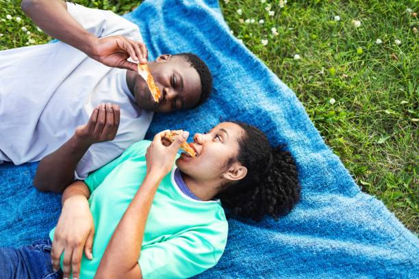 Cheerful millennial woman passing a bowl of healthy food to her friend during a picnic lunch in a park