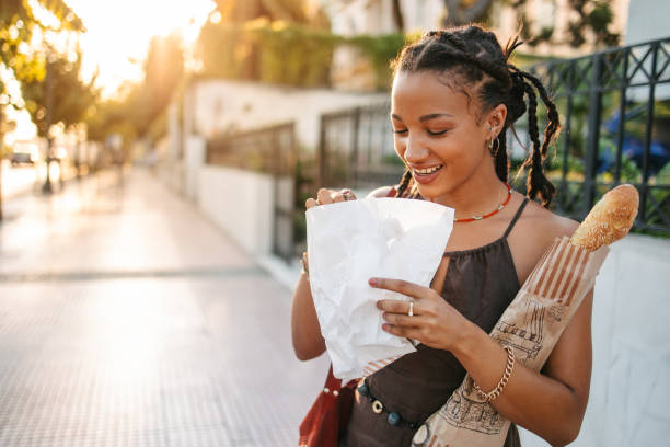 African woman eating a pretzel and holding a baguette stock photo
