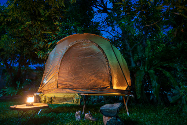 istock Camping tent and lantern with wooden table in a forest  at night 2160568414