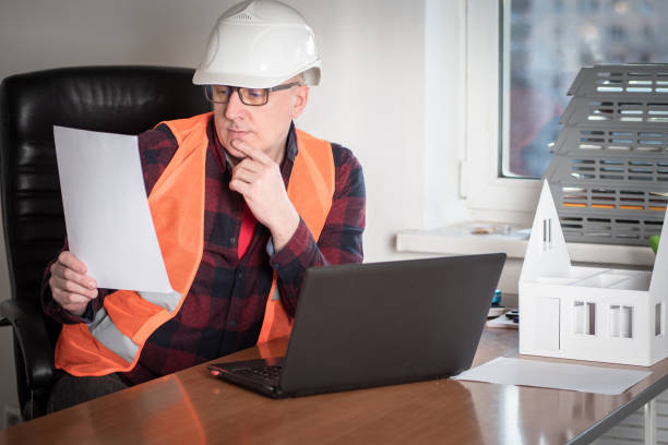 istock Work in a construction company. Work on the project of a new house. The engineer studies the document in his office. Workplace of the architect with a layout of the future cottage. 2160573624