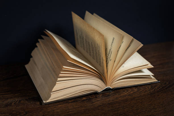 Open old book lying on a wooden table. Dark background.