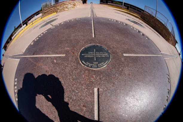 Four corners, ultra-wide-angle view of the point common to the states of Arizona, Utah, Colorado and New Mexico, photo taken straddling the Colorado/New Mexico state line, looking west towards the corner marker with Arizona and Utah beyond the monument and flags area. View is looking north so the monument is right side up and easy to read.