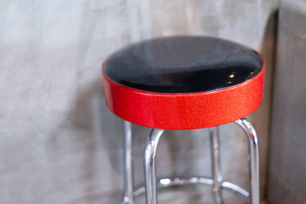 Round high bar stool with red-black leather cushion. In the background was a blurry, empty cement wall.