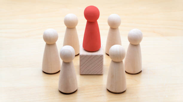 Leadership Concept with Wooden Figures This image illustrates a red wooden figure standing on a block, surrounded by natural wooden figures, symbolizing leadership and team dynamics. It represents themes such as leadership, direction, team discussion, community or social feedback, communication or announcement dialogue, business meetings, teamwork, and communication concepts. The clear and minimalist design makes it ideal for business presentations, educational materials, and articles related to leadership and organizational structures round wooden chair stock pictures, royalty-free photos & images