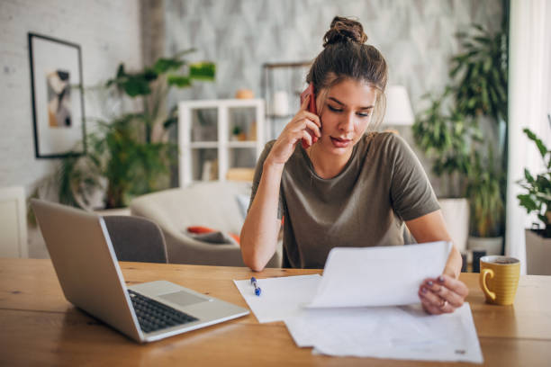 Woman on phone reviewing documents at home workspace