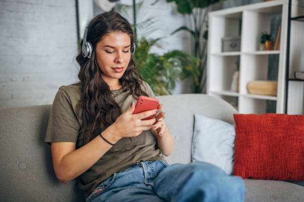 istock Woman on sofa with headphones and using smartphone 2160586246