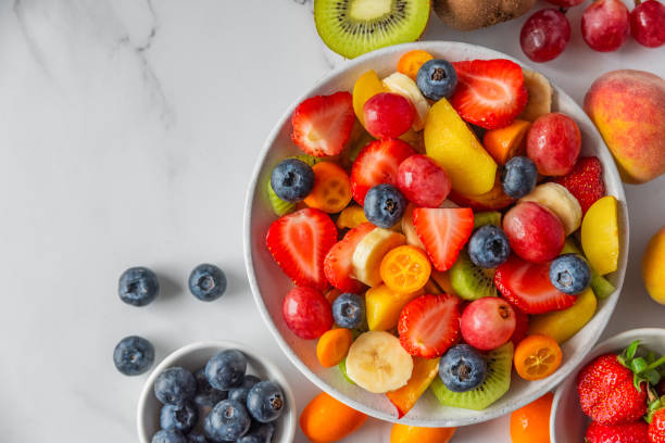 istock Summer fresh fruit salad in a bowl on white marble background. Top view with copy space. Healthy food for breakfast. Mixed strawberries, grapes, banana, kiwi, blueberries, peach, citrus for diet lunch 2160586534