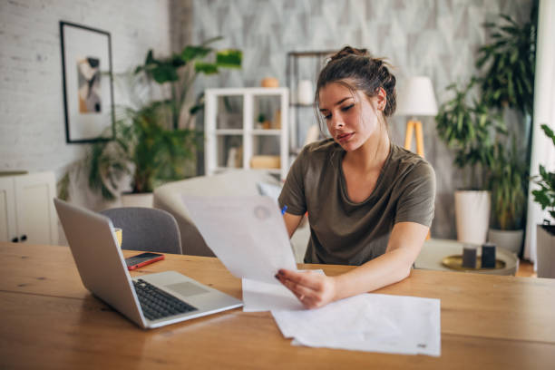 istock Woman reading documents at home with laptop nearby 2160586993