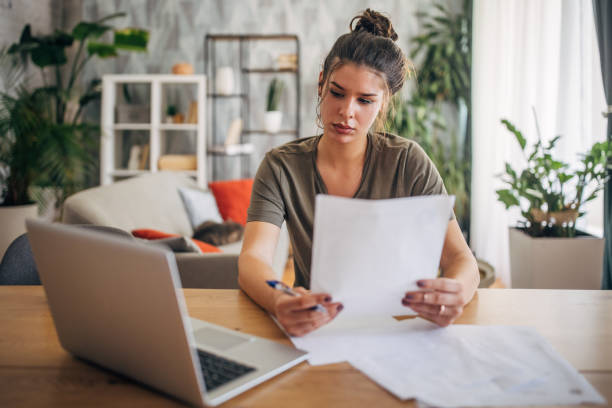 istock Woman reading paper with laptop on table beside. 2160587086