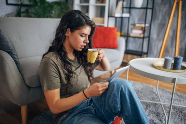istock Woman sipping coffee reading tablet, comfortable setting. 2160588532