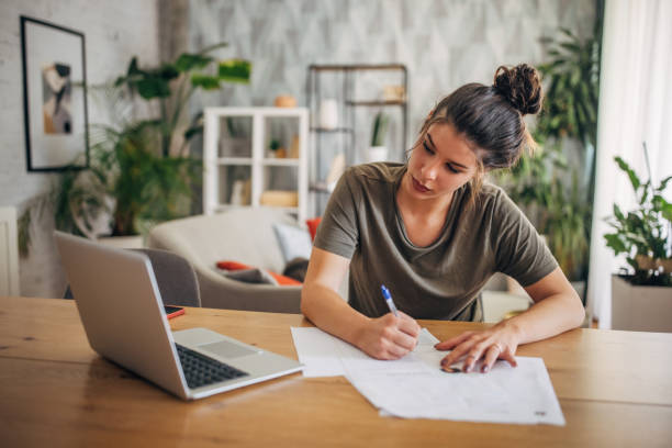 istock Dedicated woman writing on papers next to laptop. 2160589243