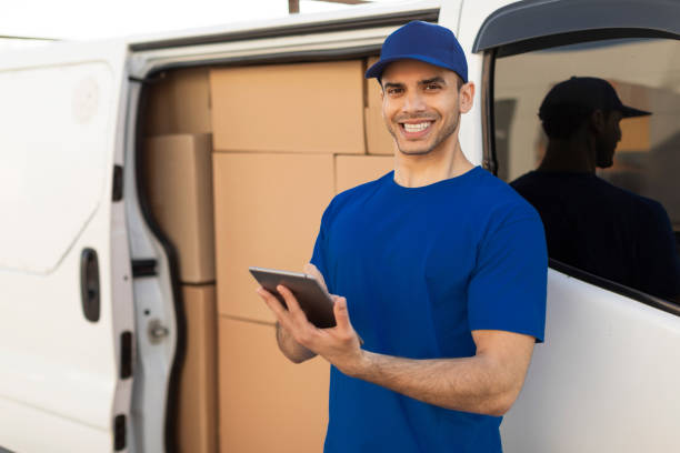 istock Delivery driver man smiling at camera beside his van full of parcel boxes, holding digital tablet, ready to drive to customers 2160591277