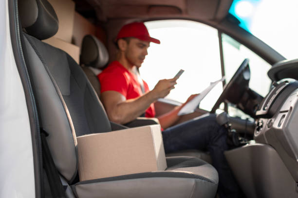 istock Courier man checking customer address using cellphone, sitting at drivers seat in van, focus on parcel nearby 2160591931