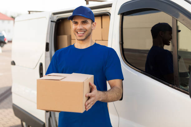 istock Mail service and shipment concept. Happy delivery man in uniform with parcel box looking and smiling at camera standing outdoors near van 2160592739