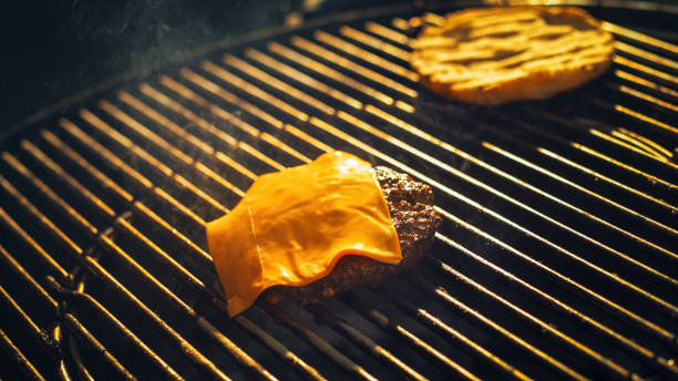 Juicy Cheeseburger Patty With Melted Cheese Sizzles on Hot Grill, Epitomizing the Essence of Outdoor Barbecue, Smoky Flavors, and Culinary Delight in Dynamic, Flame-filled Setting.
