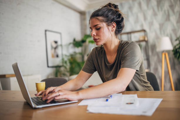 istock Woman typing on laptop at table with papers spread out. 2160594623