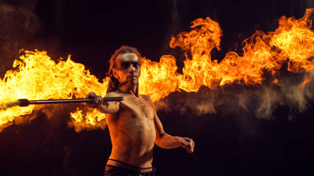 istock Shirtless Male Fire Performer With Dreadlocks Wields Flaming Staff, Creating Mesmerizing Display of Fire and Sparks Against Dark Background,  His Intense Skill and Artistry in Fire Manipulation. 2160594652