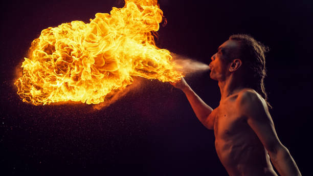 istock Shirtless Male Fire Performer With Dreadlocks Expertly Breathes Massive Fireball, Creating Captivating Display of Flames and Sparks Against Dark Background,  His Skill and Artistry in Fire Breathing. 2160594664