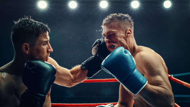 istock Two Male Boxers Exchange Powerful Punches in an Intense Match Under Bright Lights,  Raw Strength and Fierce Competition in the Ring. Sweat and Determination in High-energy Sport. Boxing Championship 2160594921