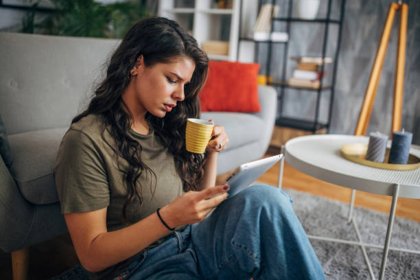 istock Woman with yellow coffee mug reading on tablet. 2160595227