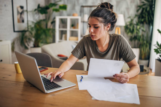 Woman working on laptop with papers at a table.