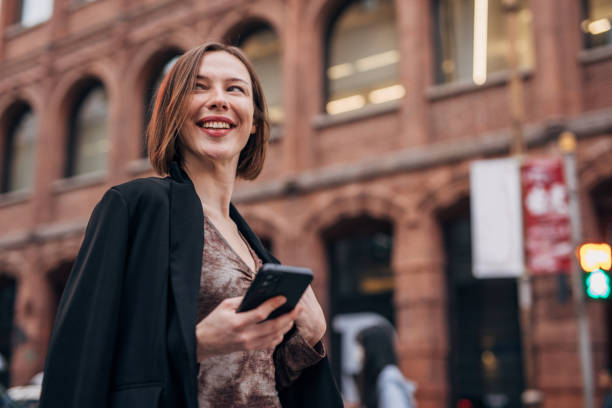 istock Happy woman standing outdoors holding smartphone 2160597146