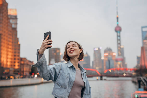istock Woman taking selfie by river with city skyline backdrop 2160599629