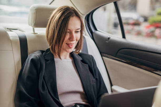 istock Woman working on laptop, car interior with leather seats 2160600553