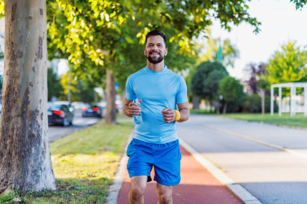 istock Active man jogs with water bottle in sunny park. 2160609836