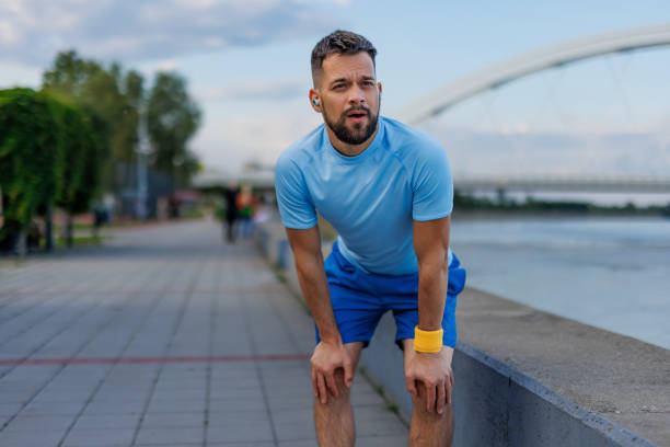 istock Man bending over after workout by river and bridge 2160610396