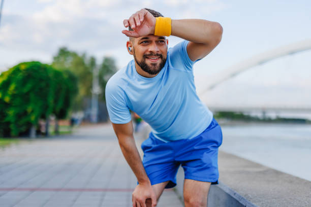 istock Man wiping forehead after exercise by river and bridge 2160610412