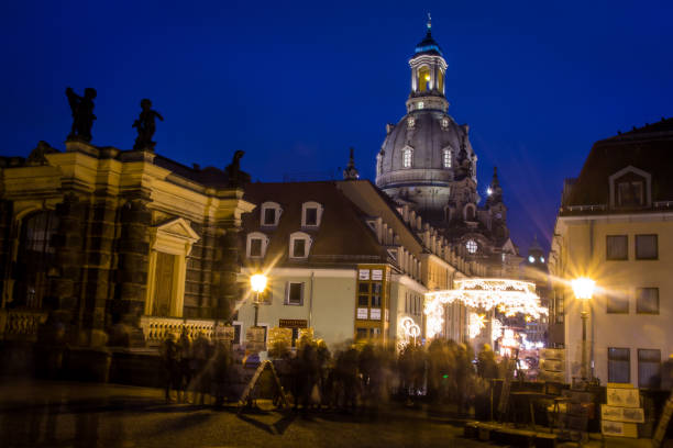 A classic city view featuring a baroque church dome rising above elegant historic façades in Dresden. An ornate street lamp adds depth and character to the composition under a clear blue sky. Ideal for themes of European architecture, travel, heritage, and urban history.