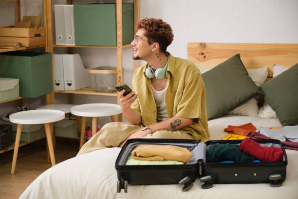 istock Young man is packing for a trip and checking his phone 2160611240