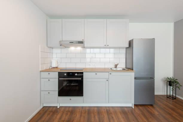istock Scandinavian Style Cozy Modern Open Bright Minimalism Kitchen Home Interior. Oven, Faucet, Kettle, Fridge and Furniture in Background. Dark Brown Flooring. Flower. White Cabinets 2160611519