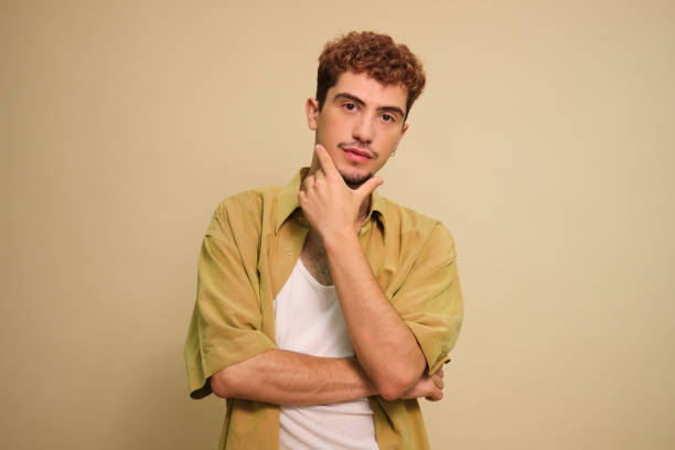 istock Young man with hand on chin thinking and looking at camera 2160611659