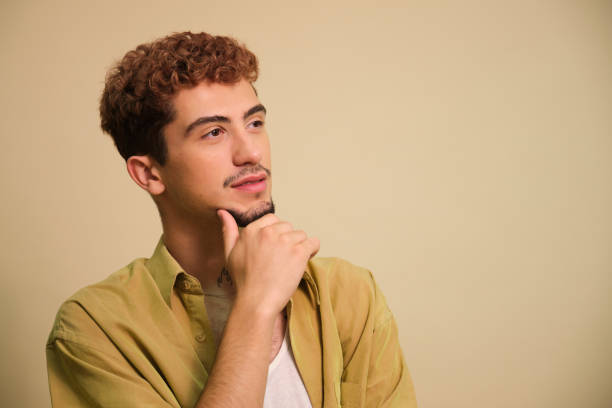 istock Thoughtful young man touching chin looking up on neutral background 2160613228