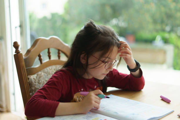 istock A little girl with glasses rested her head on her hand while solving problems from a textbook at the table. Homeschooling concept 2160614073