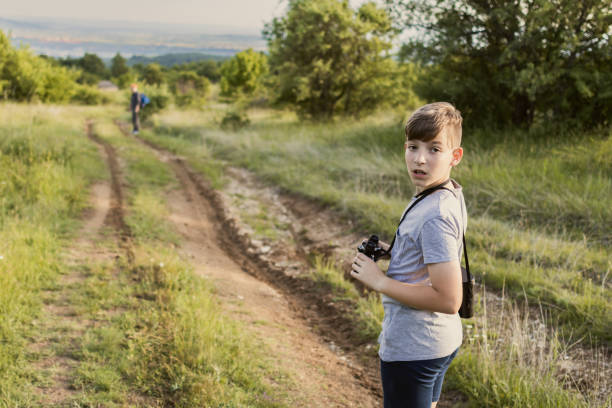 Boy is spending summer break with his grandfather on mountain. Active senior with backpack and hiking poles is hiking with his grandson. They are exploring nature with binoculars.