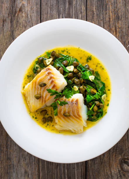 istock Fish dish - fried cod with spinach and capers in saffron sauce on wooden table 2160620878