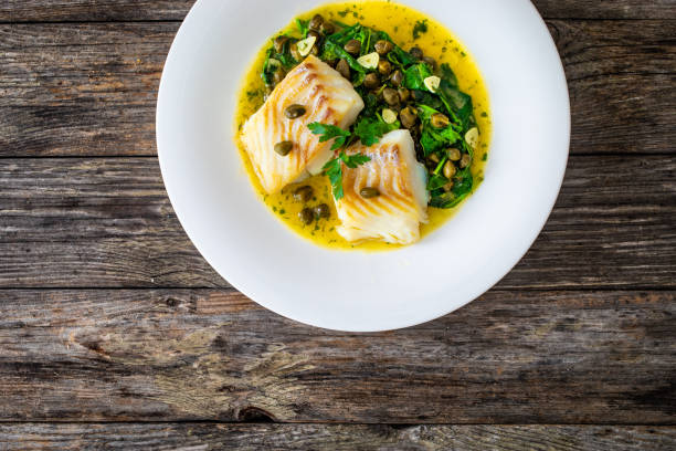 istock Fish dish - fried cod with spinach and capers in saffron sauce on wooden table 2160620896