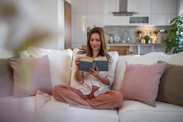 istock A woman sits on her favorite sofa, enjoying a peaceful moment while reading a book 2160622002