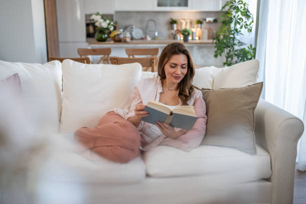 istock A woman sits on her favorite sofa, enjoying a peaceful moment while reading a book 2160622093