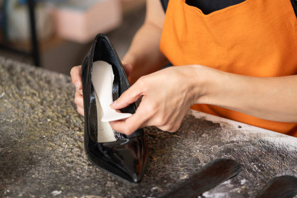 istock Young Woman in Orange Apron at Workbench in Shoe Workshop 2160630584