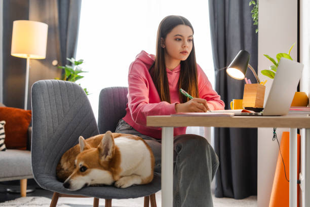 istock Focused female student taking notes while studying online with dog sleeping nearby 2160632024
