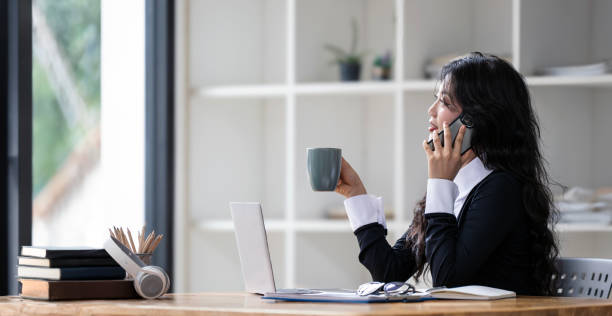 istock Pretty businesswoman using mobile phone and drink coffee white working with laptop at table in office 2160657426