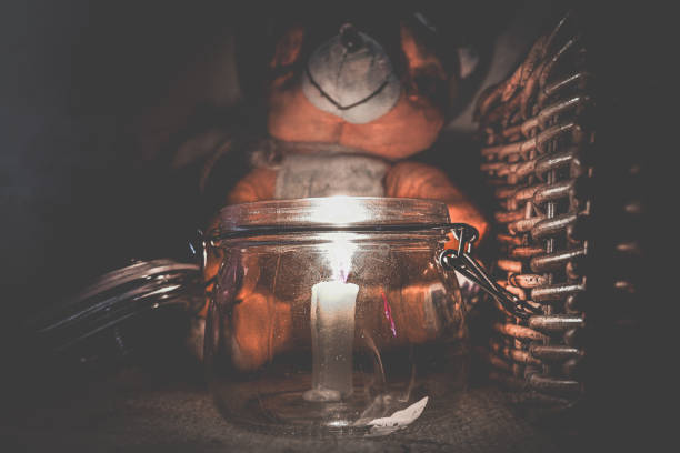 A teddy bear and a candle burning in the dark