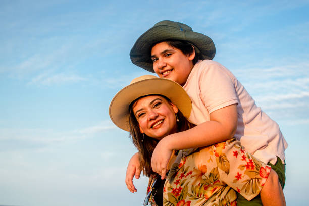 istock Latin woman carrying her son on her back, both with hats on the beach 2160677112