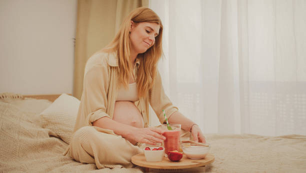 istock A pregnant woman sits on the bed and eats breakfast. 2160677309