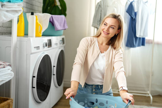 istock Woman Folding Laundry in a White Room With a Blue Laundry Basket 2160679156