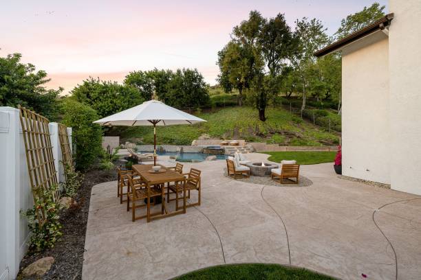 istock A backyard with a patio, outdoor dining set, fire pit, and swimming pool surrounded by lush greenery 2160683303